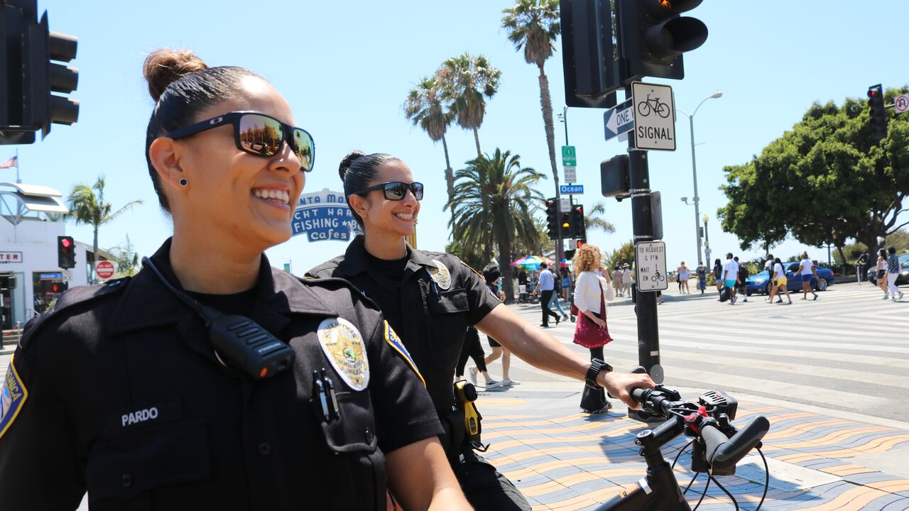 Two female police officers smile near the Pier sign with a bicycle