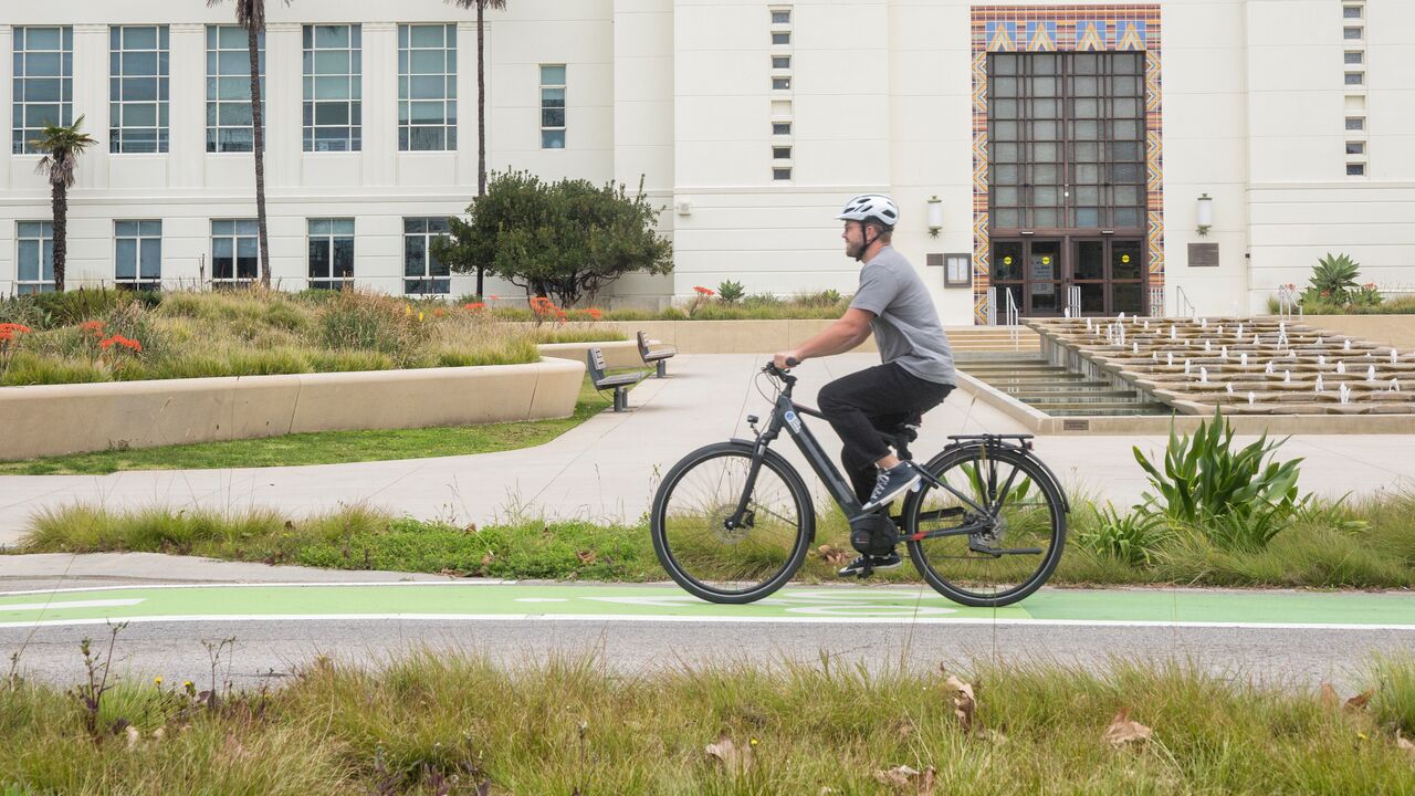 Cyclist wearing a helmet and riding in bike lane using Gazelle brand pedal-assist e-bike with Santa Monica City Hall in the background