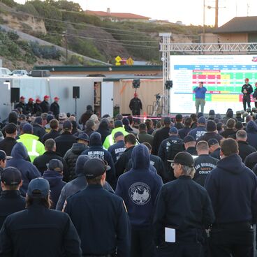 Crowd of first responders watch a presenter on stage at the command post for Palisades Fire