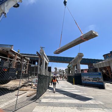 A suspended beam with the partially demolished Pier Bridge in the background during Pier Bridge Replacement Project