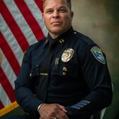 Captain Lowell Watson wearing a police uniform sitting with an American Flag behind him