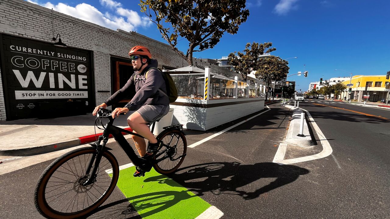 Man wearing a helmet rides a bicycle in a protected bike lane near Bodega Wine Bar on Broadway