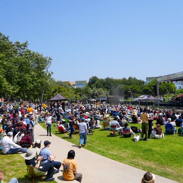 People sit on the grass in front of a music stage at Tongva Park