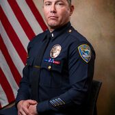Captain Robert D'Andrea wearing a police uniform sitting with an American Flag behind him