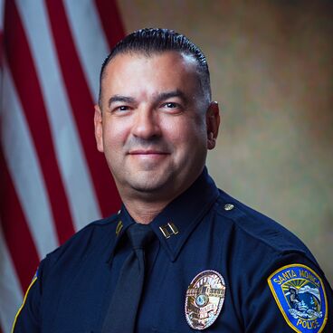 Police Captain Roberto Villegas in Uniform With a Flag Behind Him