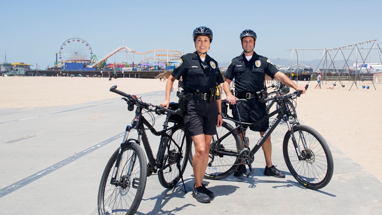 Two Police Officers with Bikes and Helmets on the Bike Path with Santa Monica Pier in the Background