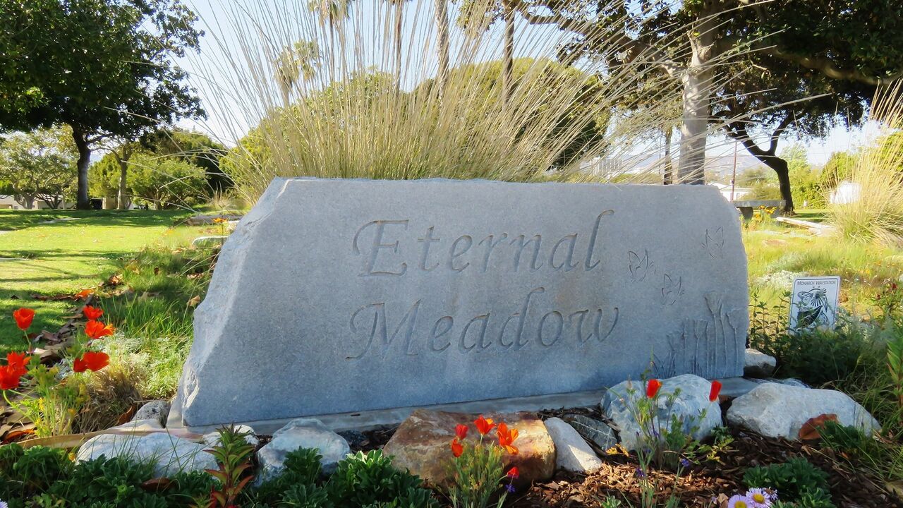 Eternal Meadows sign at Woodlawn Cemetery surrounded by flowers, stones, and greenery
