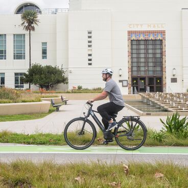 Cyclist wearing a helmet and riding in bike lane using Gazelle brand pedal-assist e-bike with Santa Monica City Hall in the background