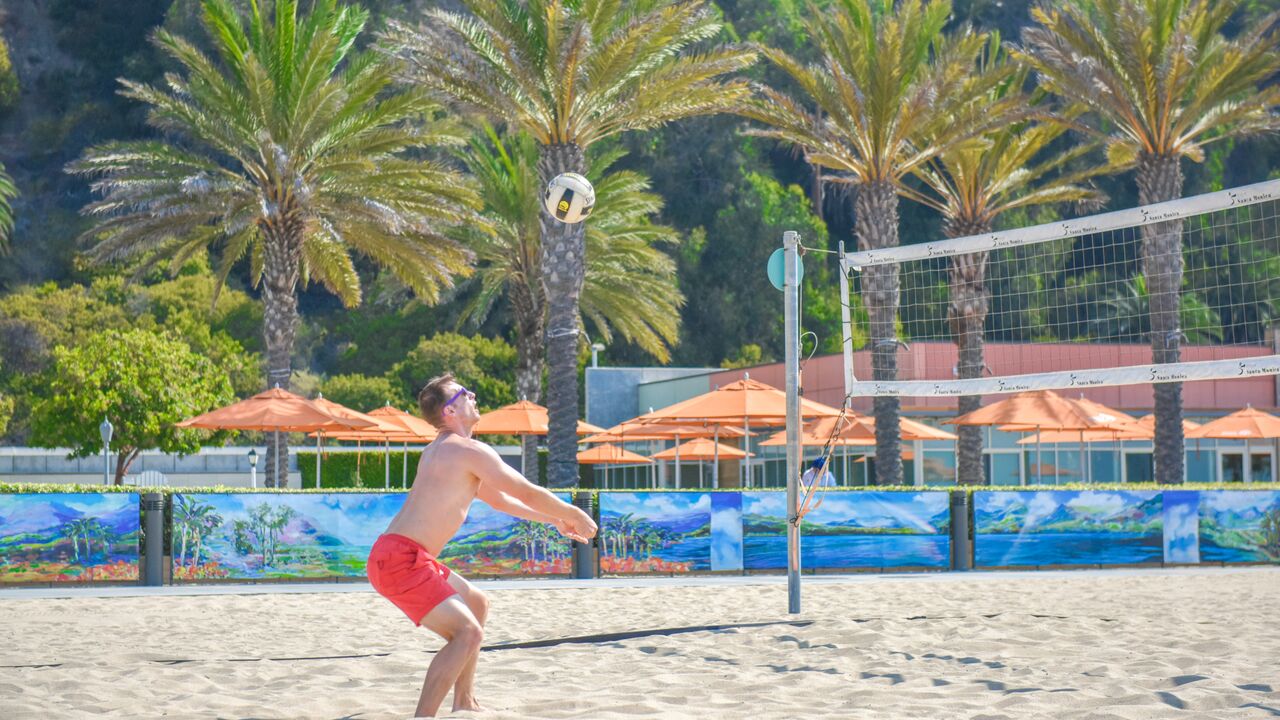 Volleyball player with ball in air with Annenberg Community Beach House in background