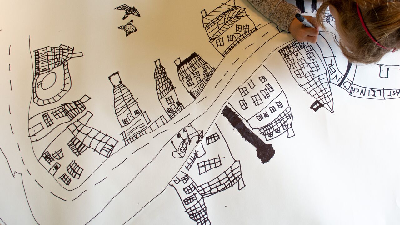 A student at Palisades Preschool draws streets and buildings on paper