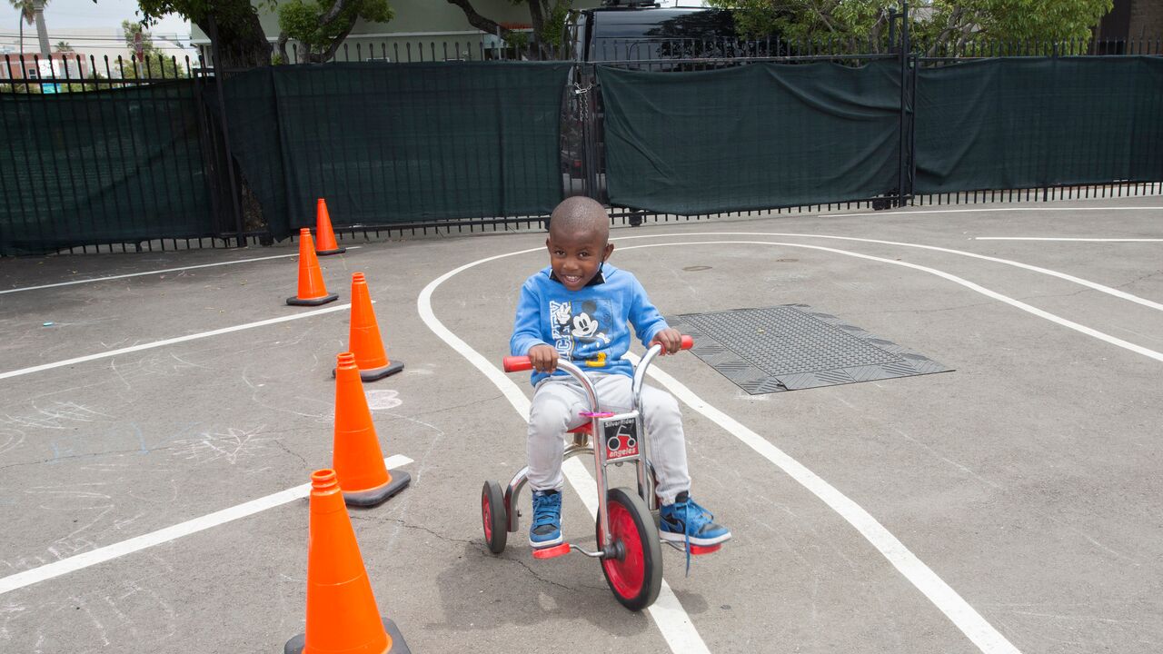 Child riding tricycle on an asphalt track next to traffic cones at Beach Moms Child Development Center 