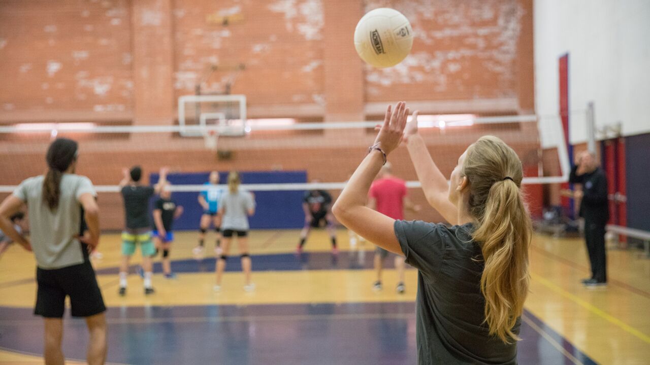 Person serving a volleyball at Memorial Park gym during an adult volleyball league game