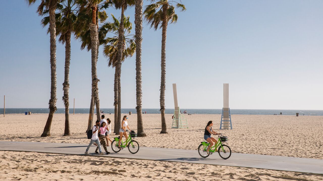 People Riding Bikes on the Beach Path With the Singing Chairs Behind Them