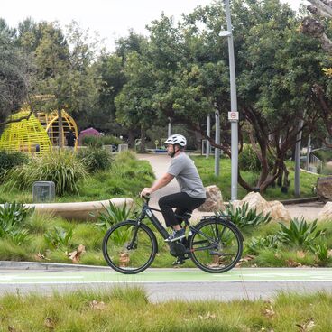 Cyclist using bike lane and wearing a helmet  using Gazelle brand pedal-assist e-bike with Tongva Park in the background