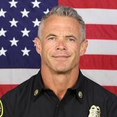 Battalion Chief Jonathan Sly in Uniform with an American Flag Behind Him