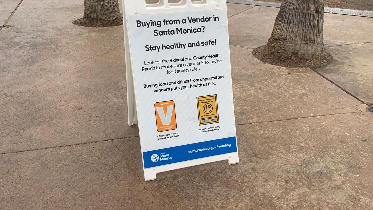 A frame sign that says that buying food and drinks from unpermitted vendors puts your health at risk and shows sample approved vendor permit from city and county