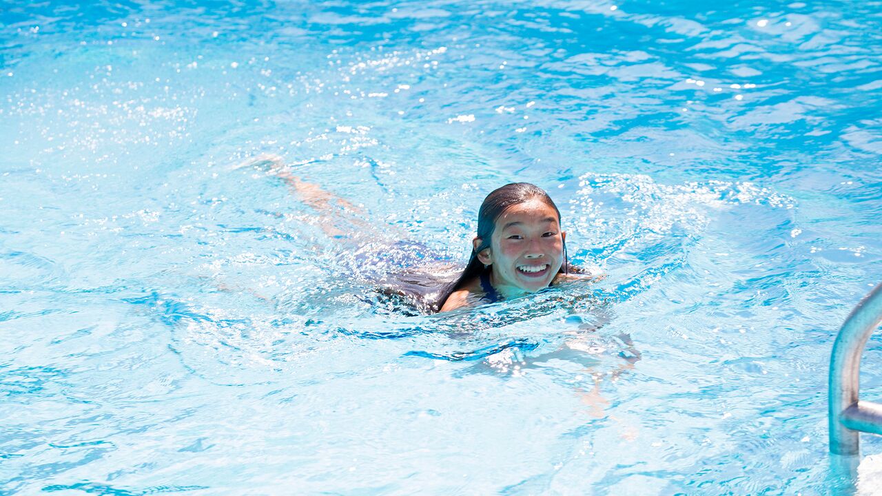 Young girl swimming and smiling at camera at the Swim Center