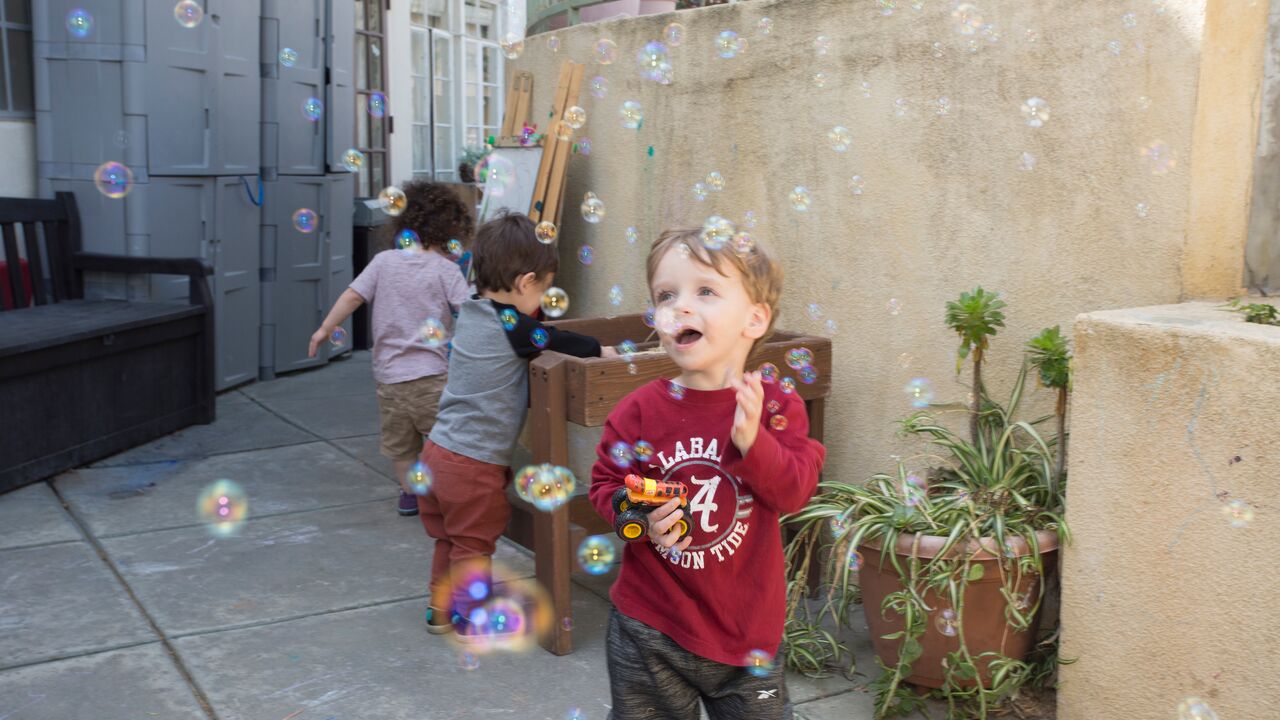 A child smiling with bubbles outdoors at Beth Shir Shalom early childhood center