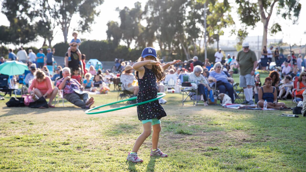 Young Girl Wearing a Dodger's Hat Hula Hooping With a Crowd of People Watching a Concert Behind Her