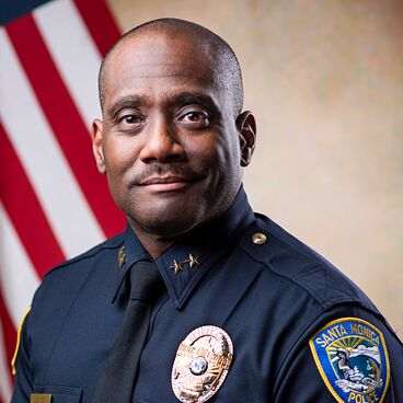 Deputy Police Chief Darrick Jacob in Uniform With a Flag Behind Him