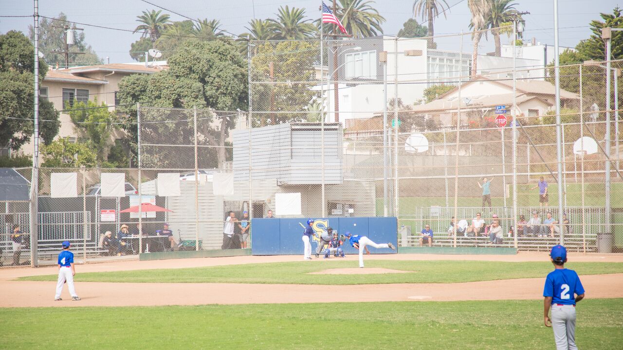 Baseball Team in Blue Playing Baseball at Los Amigos Park While Spectators Watch in the Stands