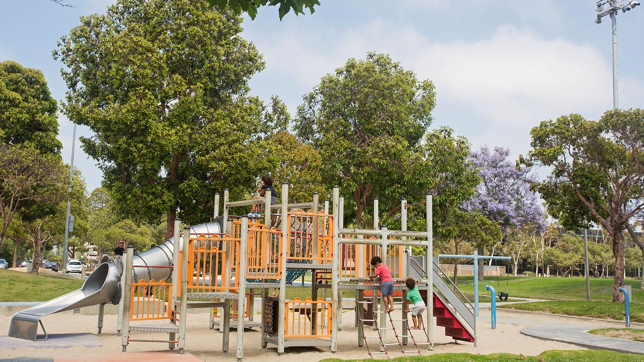 Kids Climbing on an Orange and Silver Playground With Trees Behind It
