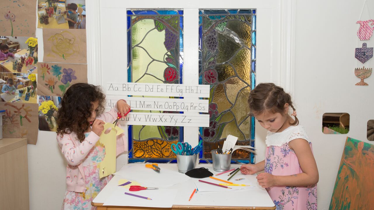 Two children at a table using scissors and paper in craft activity Beth Shir Shalom early childhood center
