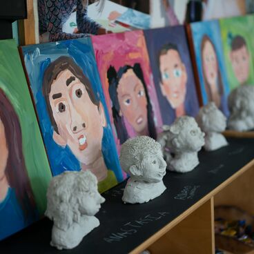 A row of self portrait paintings and sculptures made by Palisades Preschool students