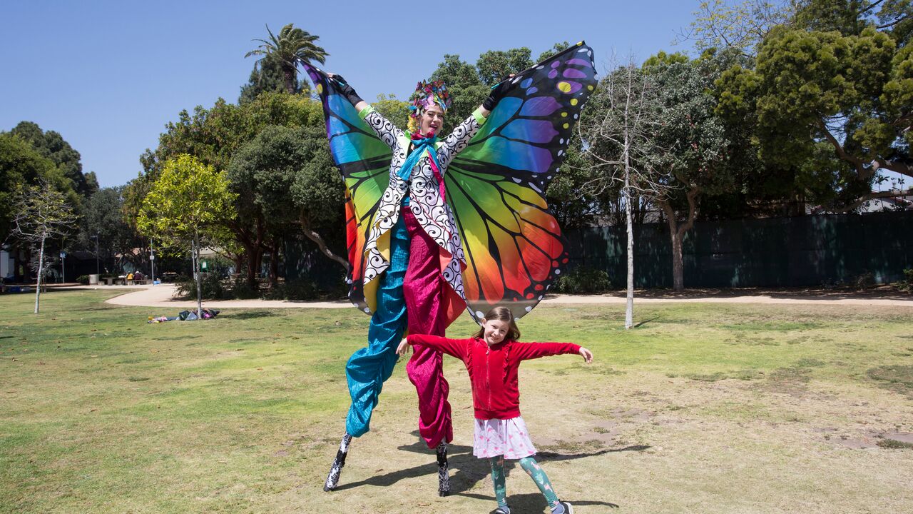 Stilt Walker Dressed as Butterfly Posing with a Child at Arts and Literacy Festival