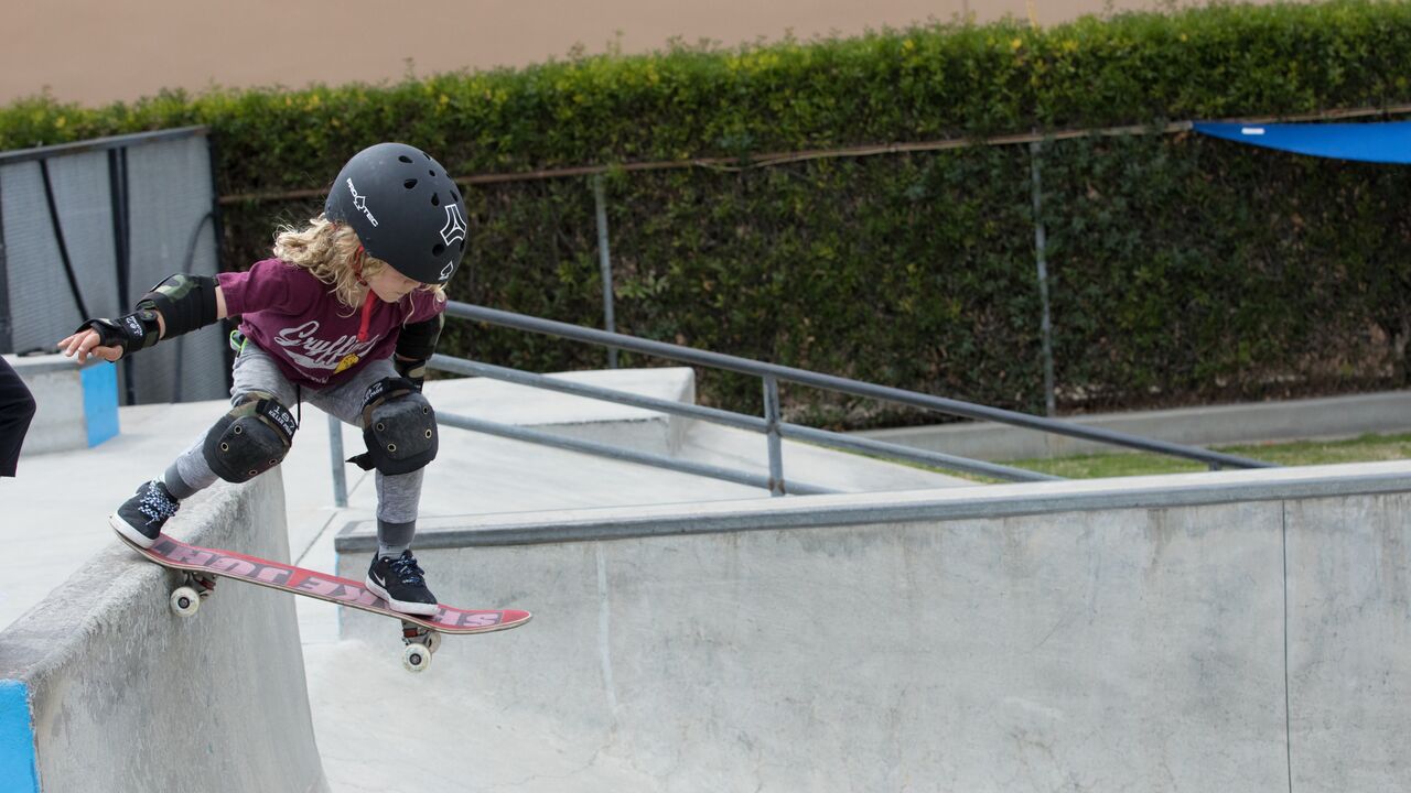 Small child wearing a helmet and protective hear and dropping into street section at Cove skatepark