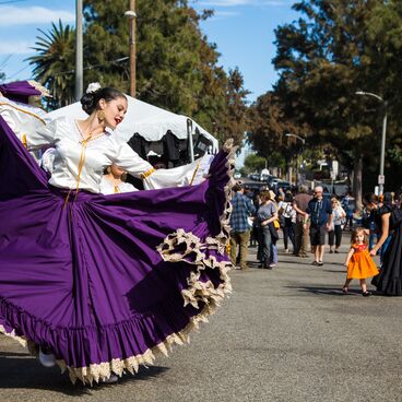 Woman in traditional Mexican clothing dancing on a street with crowds onlooking at Woodlawn Cemetery's Dia de los Muertos celebration 