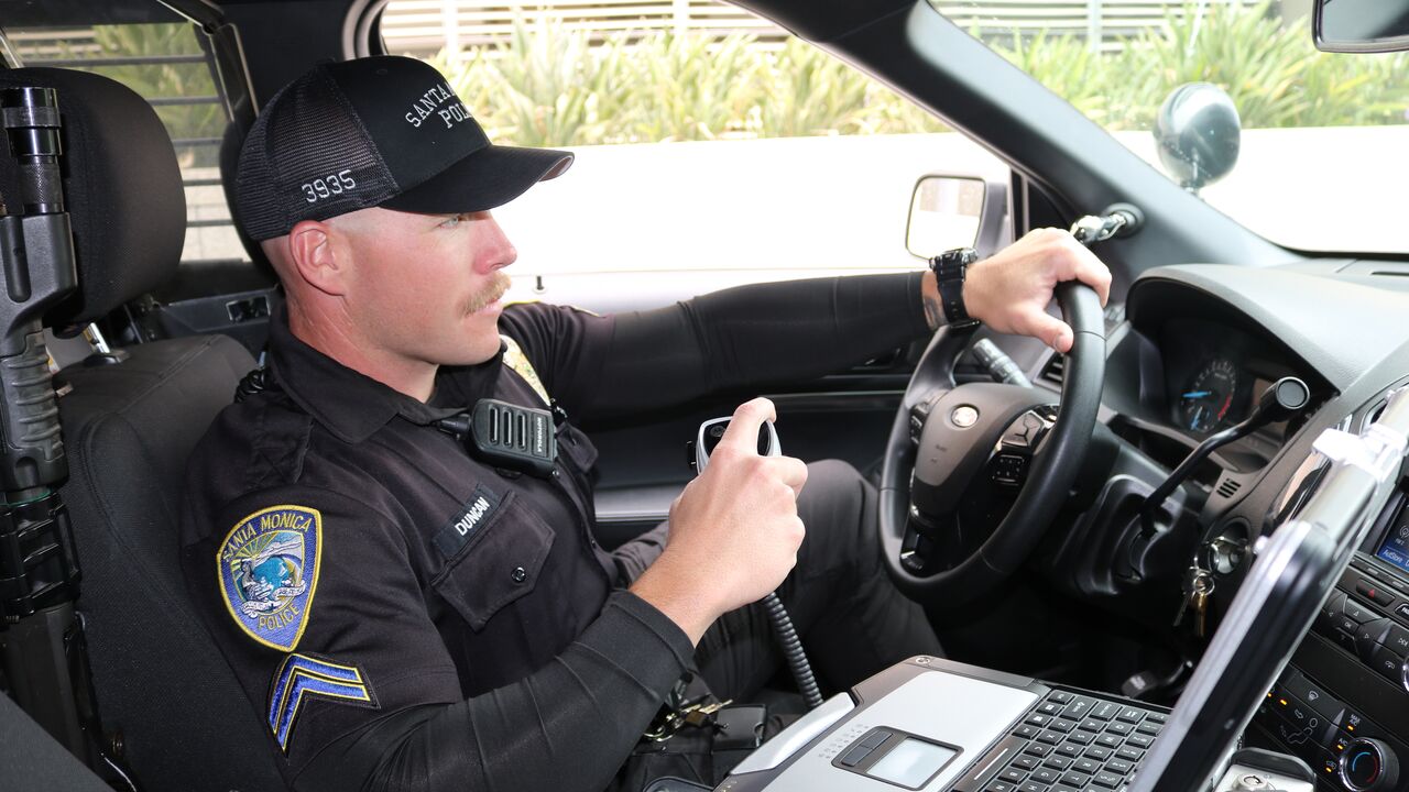 Police Officer Holding a Radio in Patrol Car