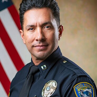 Police Captain Rudy Flores in Uniform With a Flag Behind Him