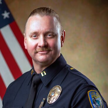 Police Captain William Heric in Uniform With a Flag Behind Him