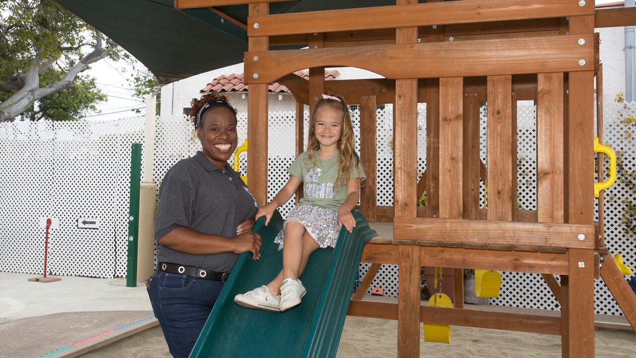 Teacher Standing next to Child on a Slide at Kidz Korner Preschool